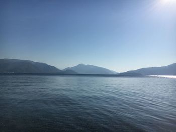 Scenic view of sea and mountains against clear blue sky