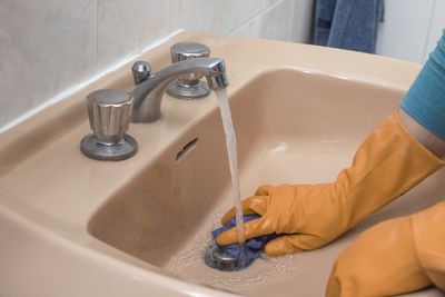 A person cleaning the bathroom sink with a glove.