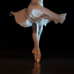 Low section of ballerina dancing against black background