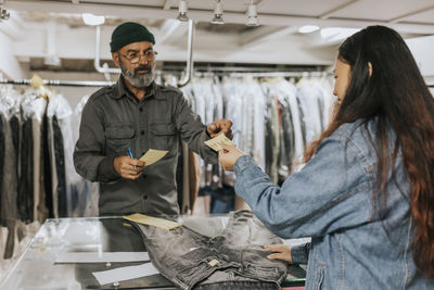 Young female customer giving bill to male tailor in workshop