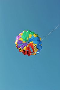 Low angle view of people parasailing against clear blue sky