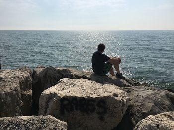 Man sitting on rock against sea at beach