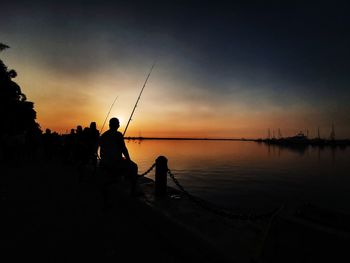 Silhouette people fishing in sea against sky during sunset