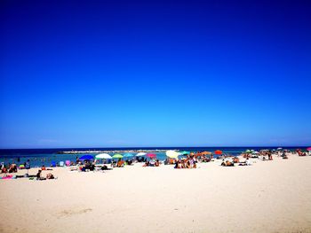 Group of people on beach against clear blue sky