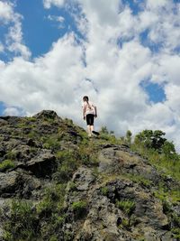 Low angle view of girl standing on rock against sky