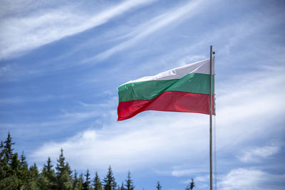 The national flag of bulgaria with few pine trees and cloudy sky in the background.