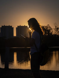 Man standing by lake against sky during sunset