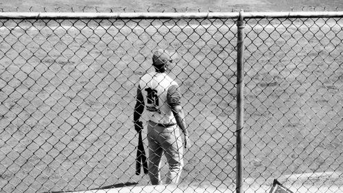 Full length of baseball player seen through chainlink fence