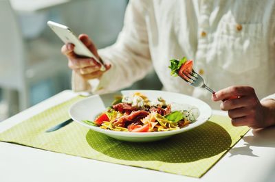 Midsection of person holding pasta and phone in restaurant