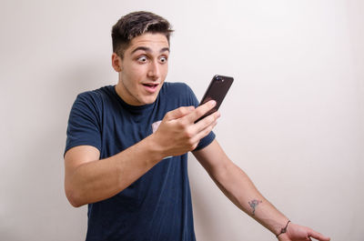 Young man using mobile phone against wall