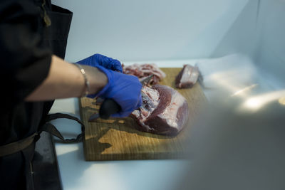 Cropped hands of woman cutting meat on cutting board at table