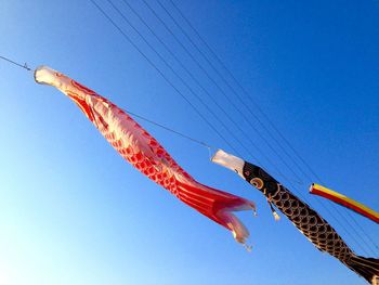 Low angle view of koinobori hanging against clear blue sky