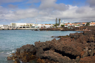 View of city at waterfront against cloudy sky