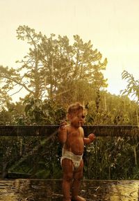 Rear view of shirtless boy on beach against sky during sunset