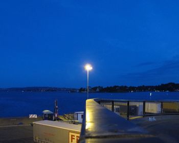 Illuminated street by sea against sky at night