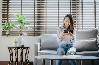 Smiling woman using phone while sitting on sofa at home