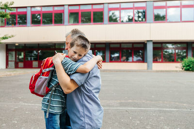 Happy dad hugs the child of the schoolboy and escorts him to school at the beginning of the lessons 