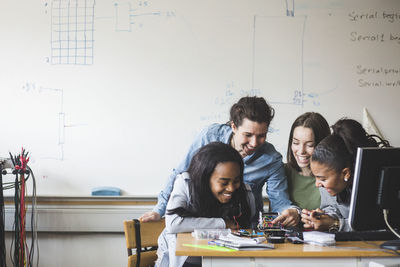 Smiling female teacher and high school teenage students preparing robot on desk in classroom