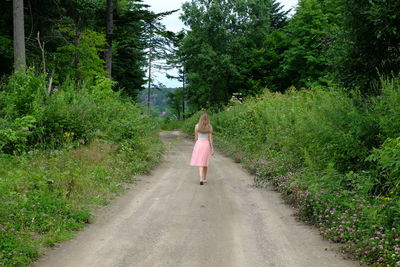 Rear view of woman walking on road amidst trees