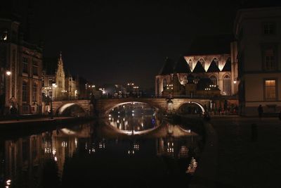 Illuminated bridge over river by buildings in city at night