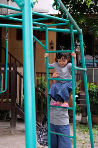 Daughter climbing on outdoor play equipment with mother at playground