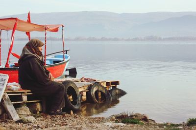 Man sitting on shore against sky