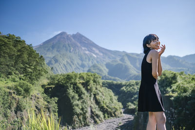 Side view of young woman standing on mountain against sky