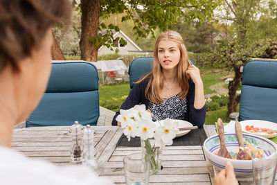 Teenage girl talking to mother at table in yard