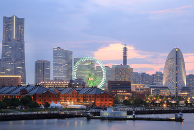 Illuminated buildings by river against sky in city