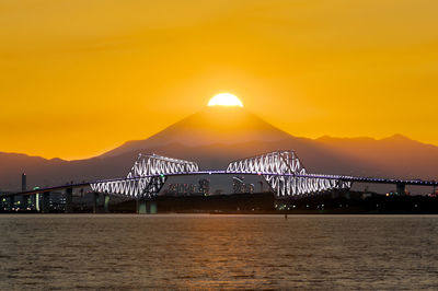 Scenic view of bridge over sea against orange sky