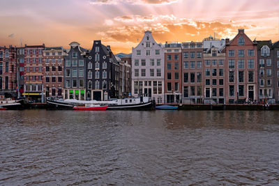 Boats in river against buildings in city at sunset