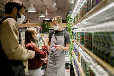 Girl talking to saleswoman by father in supermarket during covid-19