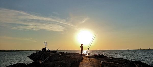 Silhouette person by sea against sky during sunset
