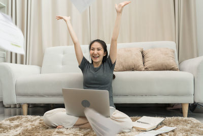 Smiling young woman using phone while sitting on sofa at home