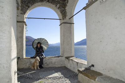 Woman sitting on retaining wall while holding umbrella by cocker spaniel