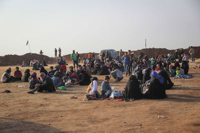 Group of people relaxing on land against clear sky