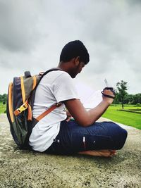 Side view of boy sitting on field against sky