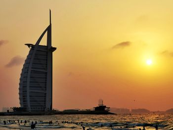 Silhouette building by sea against sky during sunset