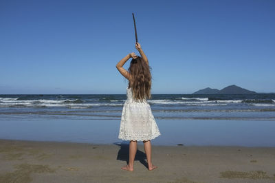 Rear view of girl standing at beach against clear blue sky