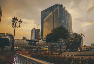 Road by buildings against sky during sunset in city