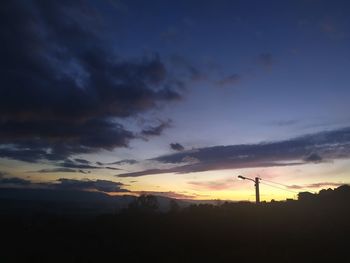 Silhouette electricity pylons against dramatic sky during sunset