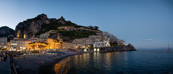 Buildings by sea against clear blue sky
