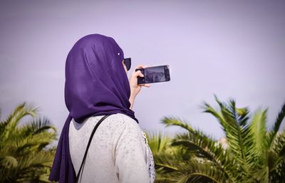 Rear view of young woman photographing with mobile phone against sky