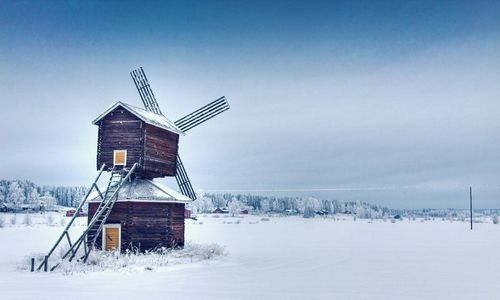 Traditional windmill on snow covered field against sky