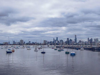 Sailboats in sea by buildings against sky