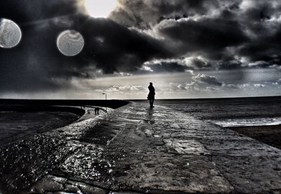 Woman standing on beach against cloudy sky