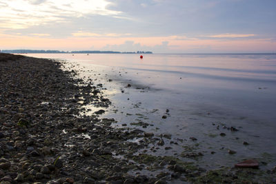 Pebbles on coast of sea with buoys floating on water