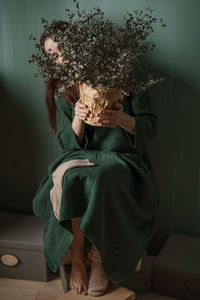 A young woman in a green linen dress making her creative self-portrait against a green wall