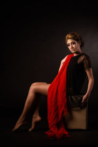 Portrait of a young woman sitting against black background