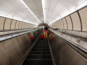 Rear view of woman with luggage standing on escalator in airport